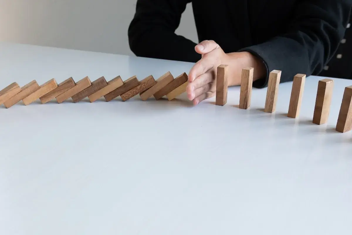 A hand stopping a row of falling dominoes before the last one topples