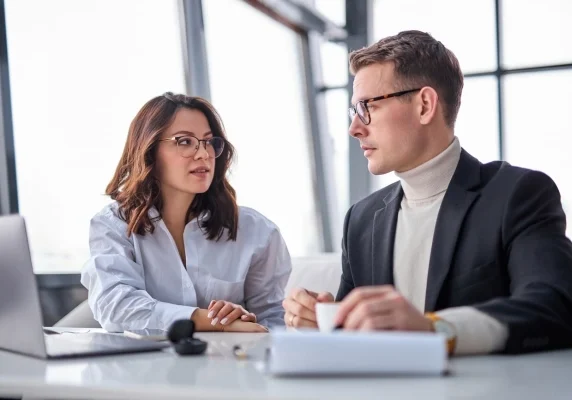 Two business partners turned toward each other in discussion at a desk