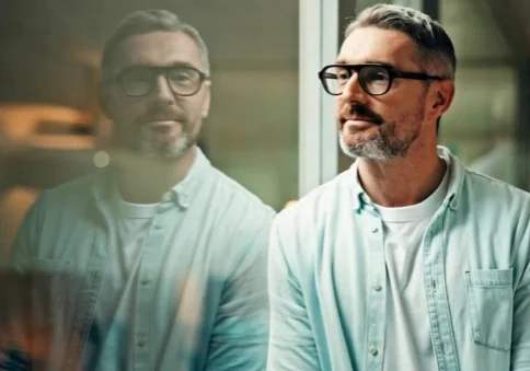 Founder standing next to a glass partition, reflecting his image, expressions unreadable